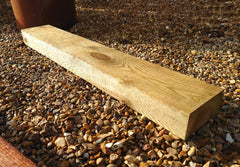 Single shot of the Green-Treated Light Brown LightGauge Timber Railway Sleeper, positioned on some stones outside.